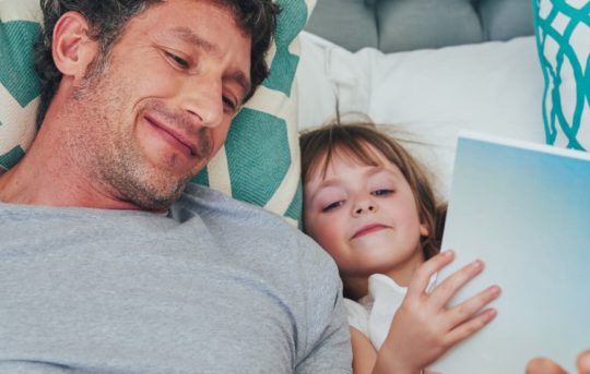 A father and daughter read in bed