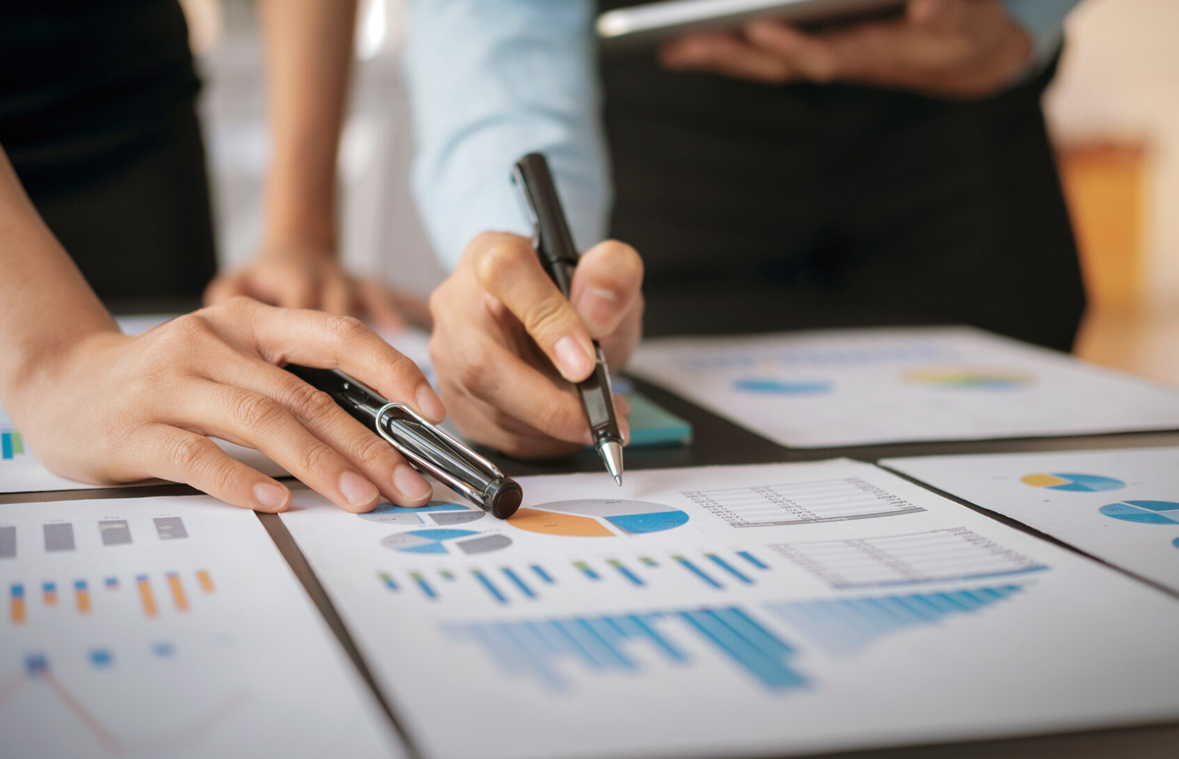 Two people holding pens point to printed financial information