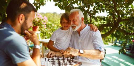 Elderly man playing chess with his grandson and son on an outdoor table