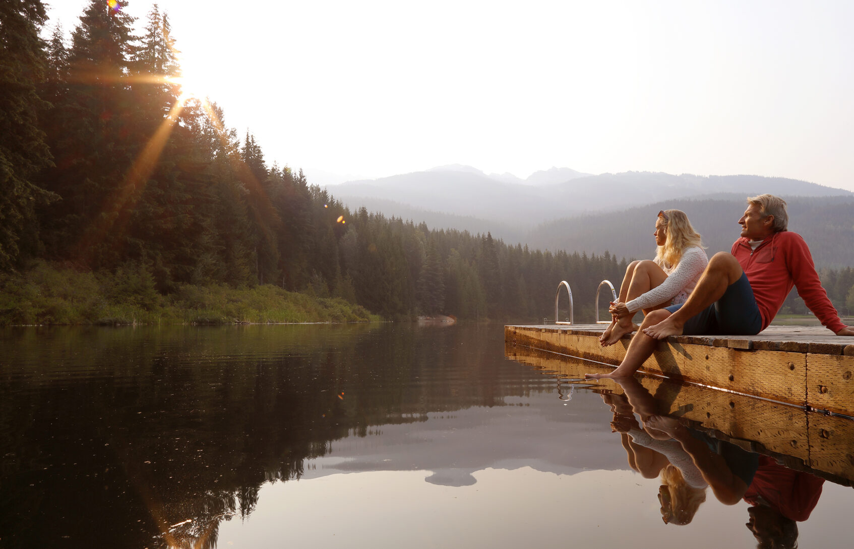 Woman and man sit on a boat dock on a lake