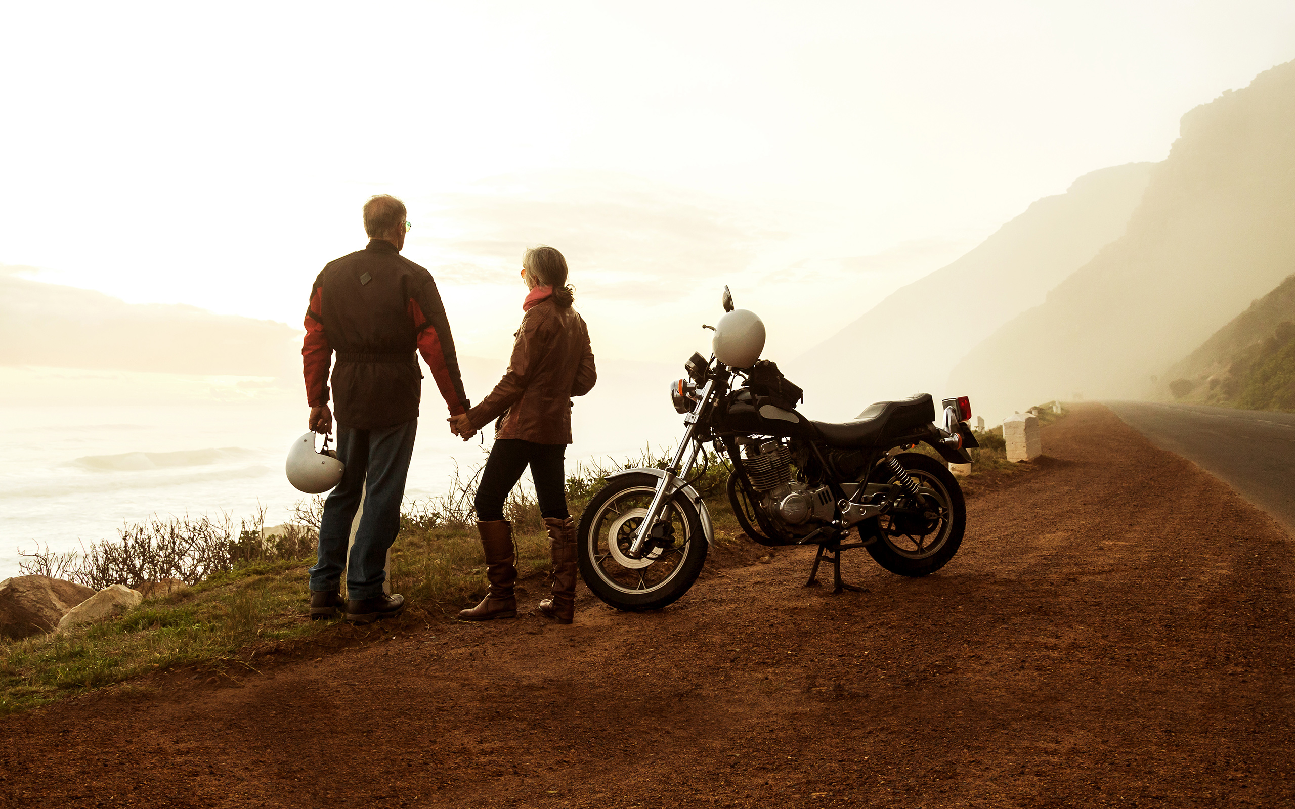 A couple stands next to a motorcycle and looks out over the horizon