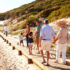 A multigenerational family walks along a wooden path on the beach