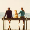 A couple and their dog sit on a dock above their reflection