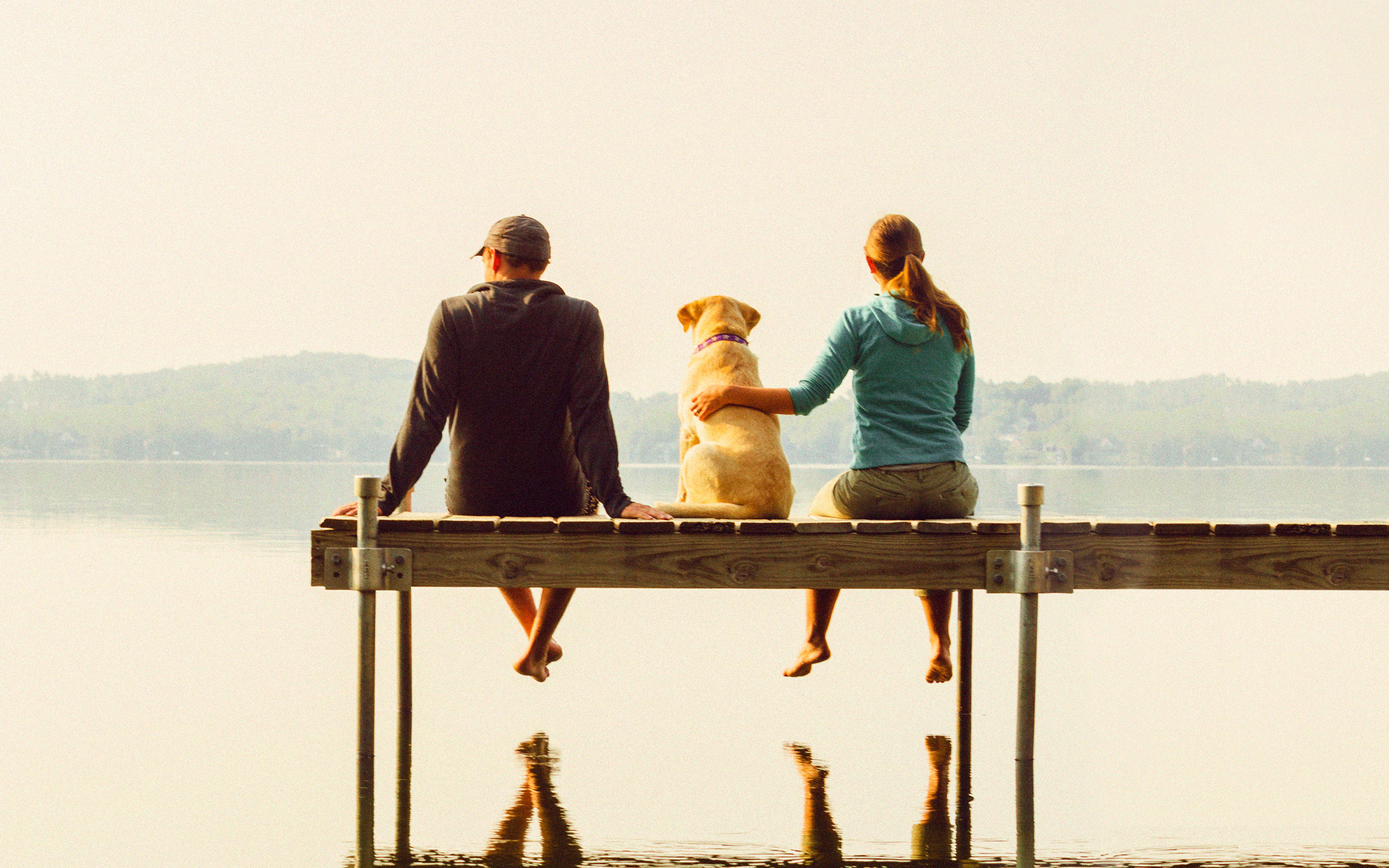 A couple and their dog sit on a dock above their reflection