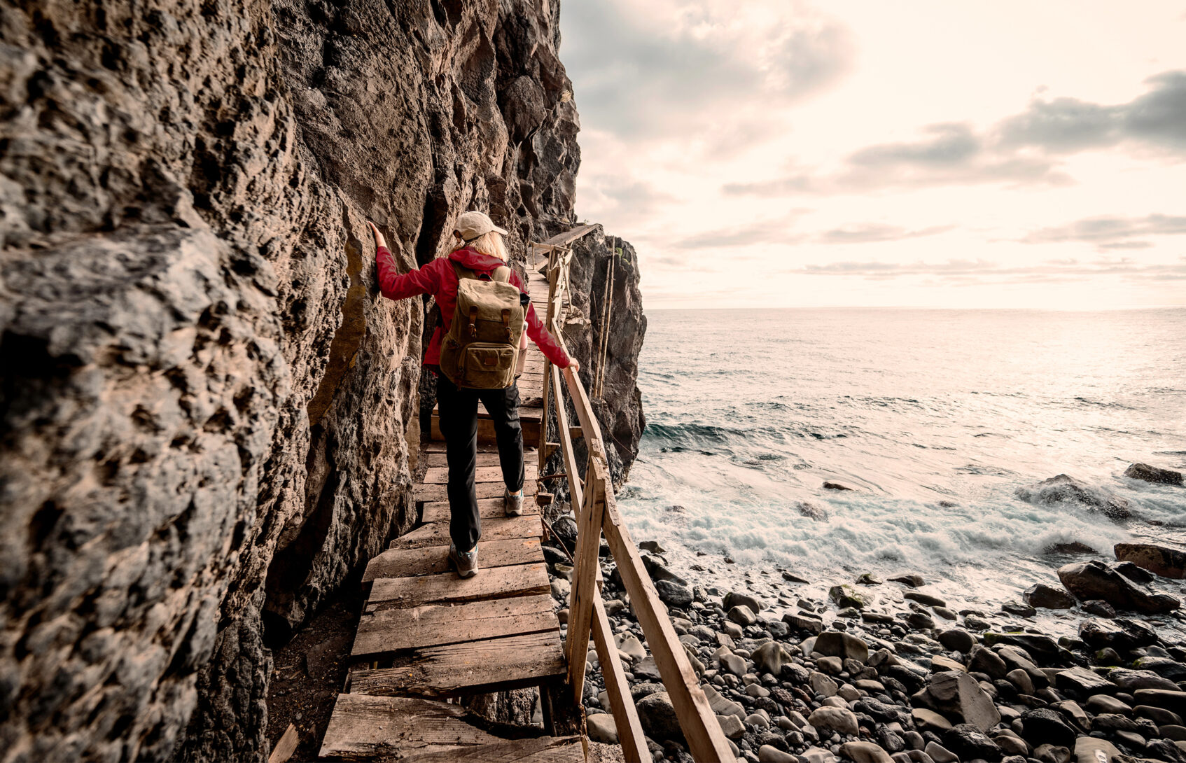 A woman uses a handrail in climbing a wooden ramp by an ocean cliff.