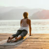 A woman stretching on a yoga mat on a dock looking out over the water.