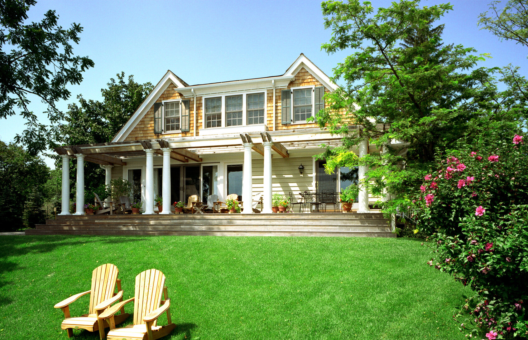 Adirondack chairs in front of a large yellow house with white columns