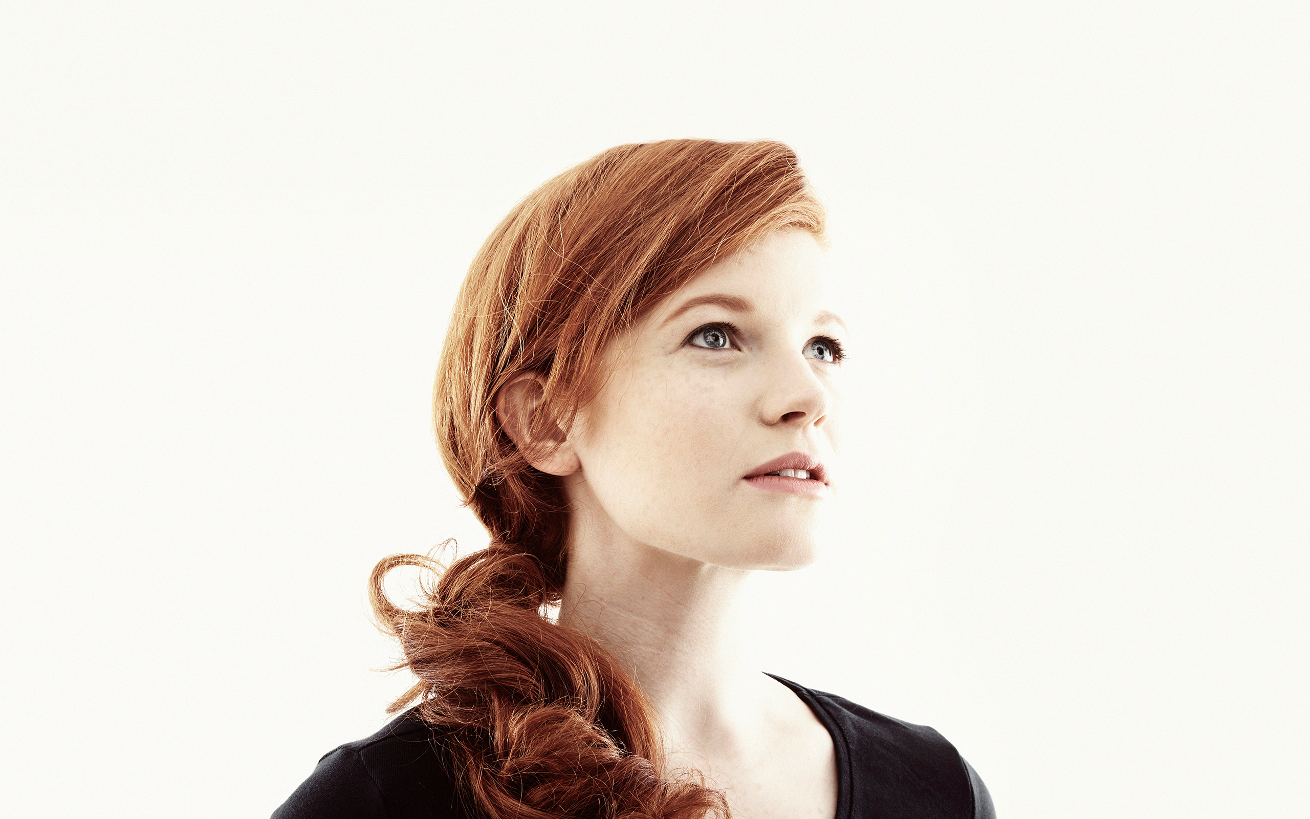 A woman in her twenties with red hair looks thoughtfully toward the sky.