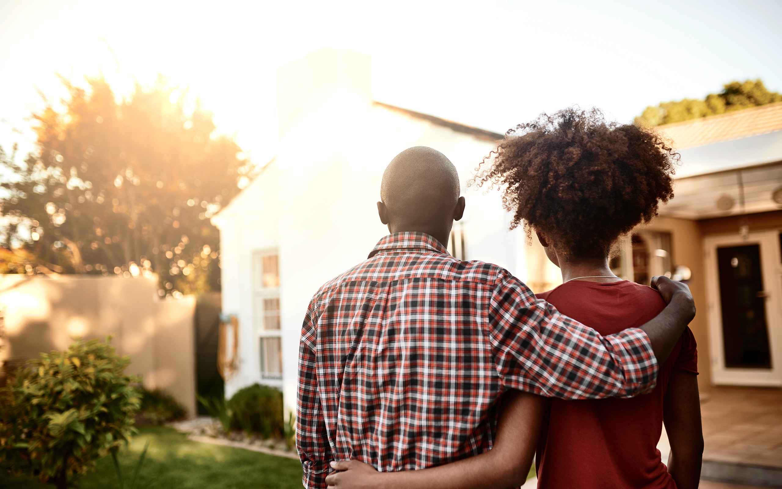A man and a woman look at a house with their arms around each other.