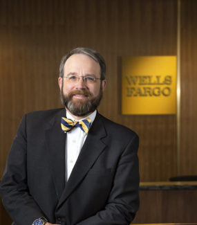 Photo of Robert G. Petix Jr. who wrote this story. He has brown hair and a beard and is wearing glasses with a suit and bowtie. He is standing in front of a Wells Fargo sign.