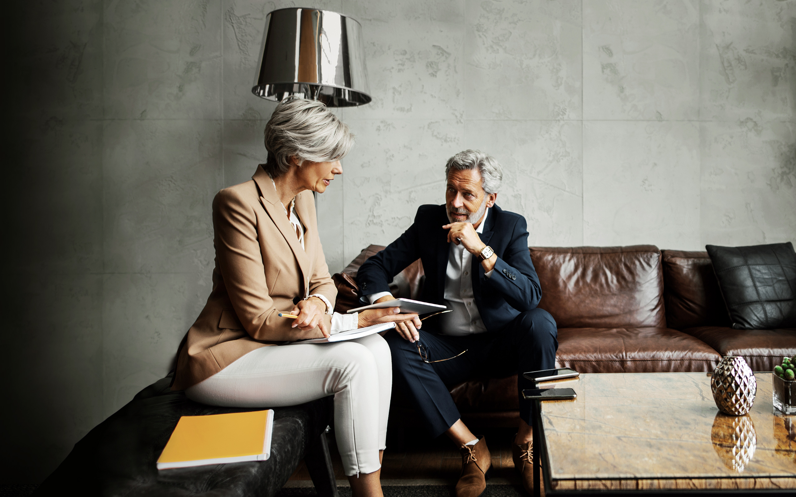 A woman advisor showing a digital tablet to a man sitting on a leather couch.