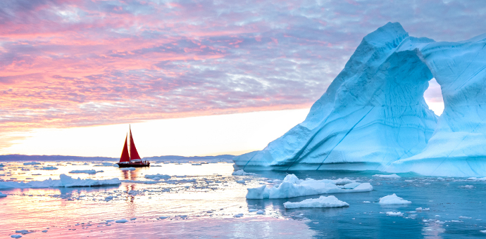 A sailboat cruises near an iceberg in Greenland