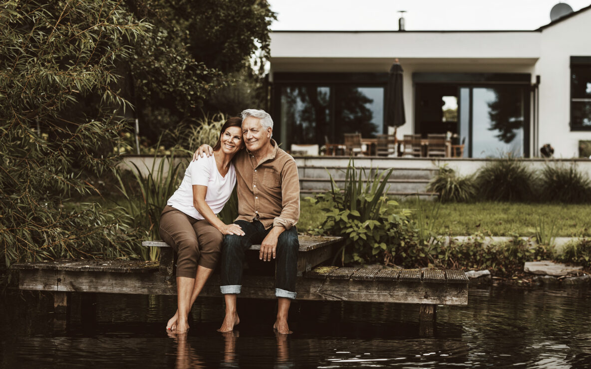 Smiling senior man sitting with arm around woman on jetty by lake
