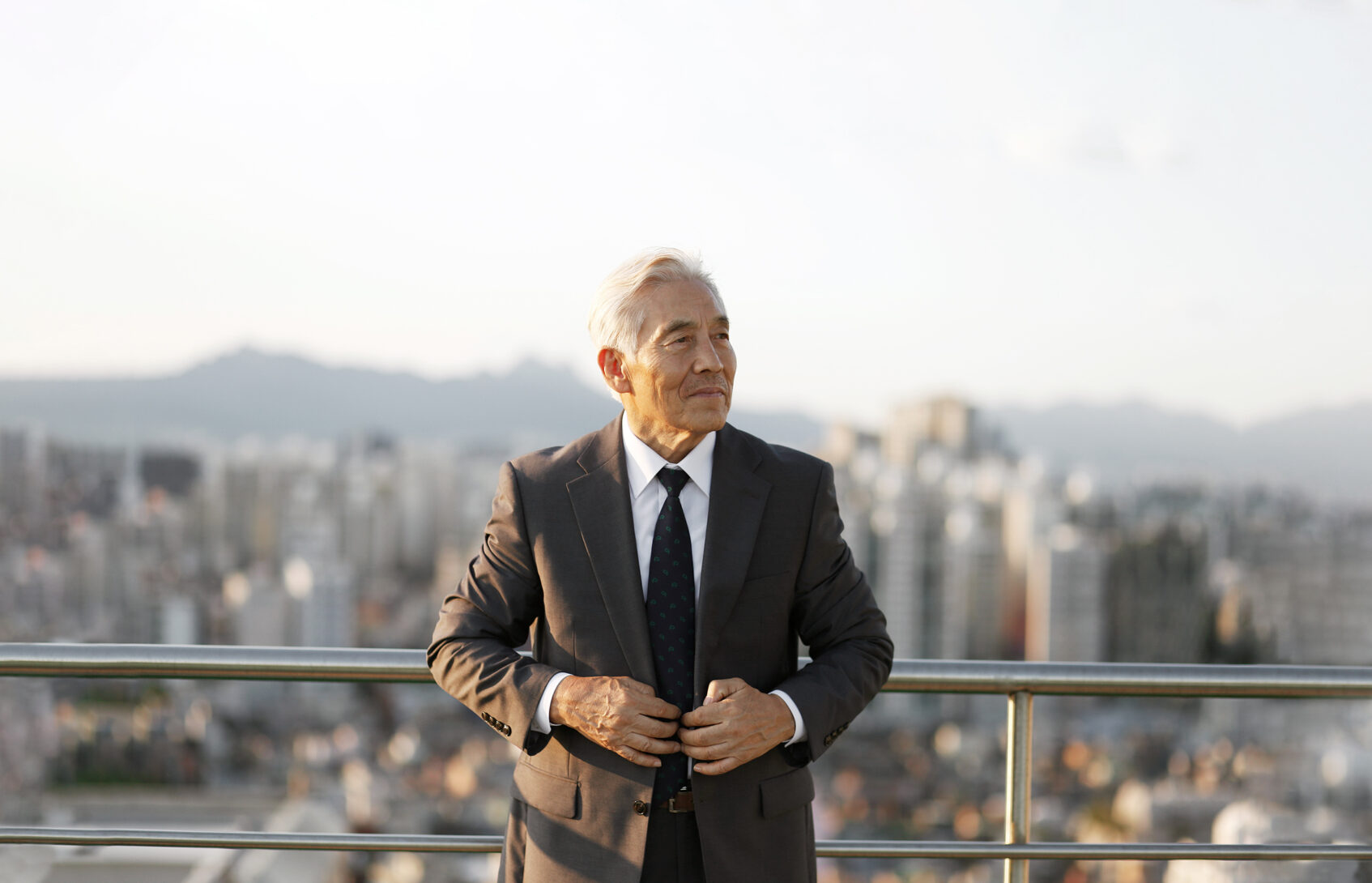 A businessman standing on balcony with city skyline in the background.