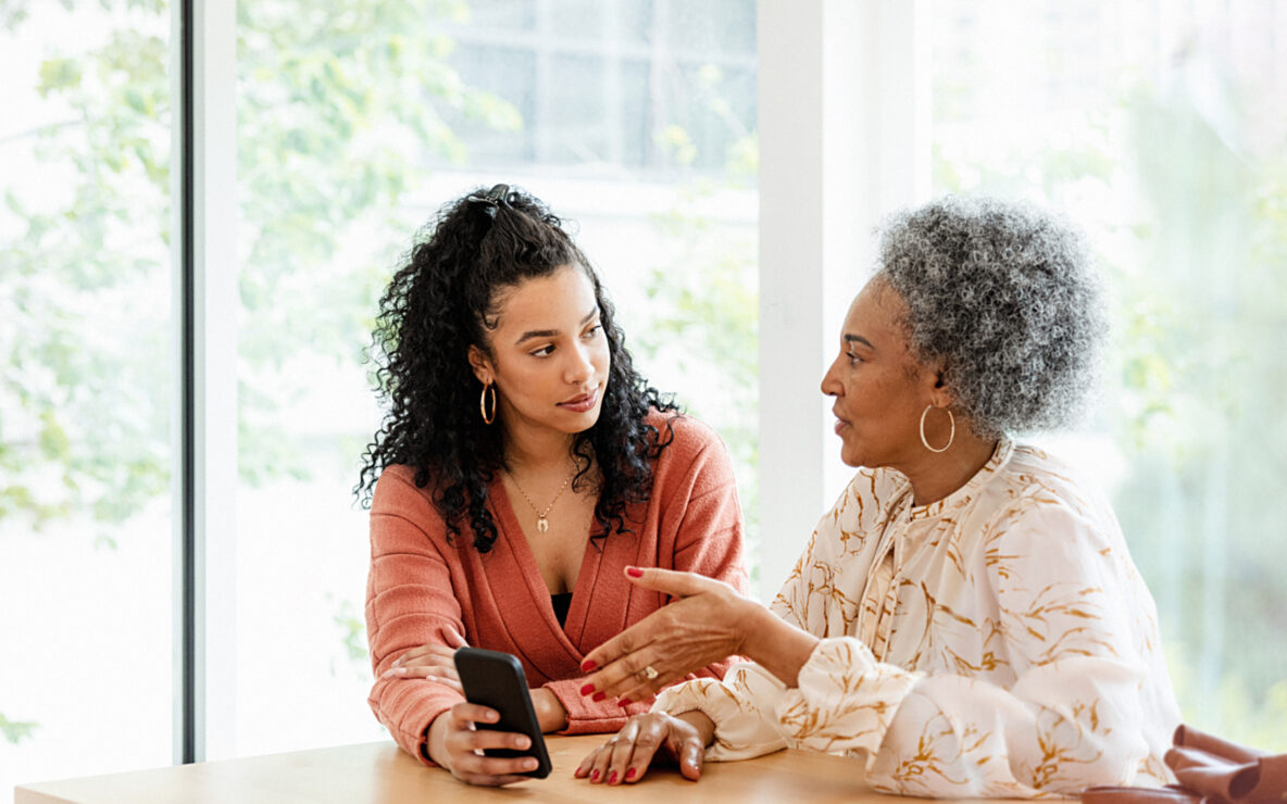 Two women seated at a table talking and holding a mobile phone