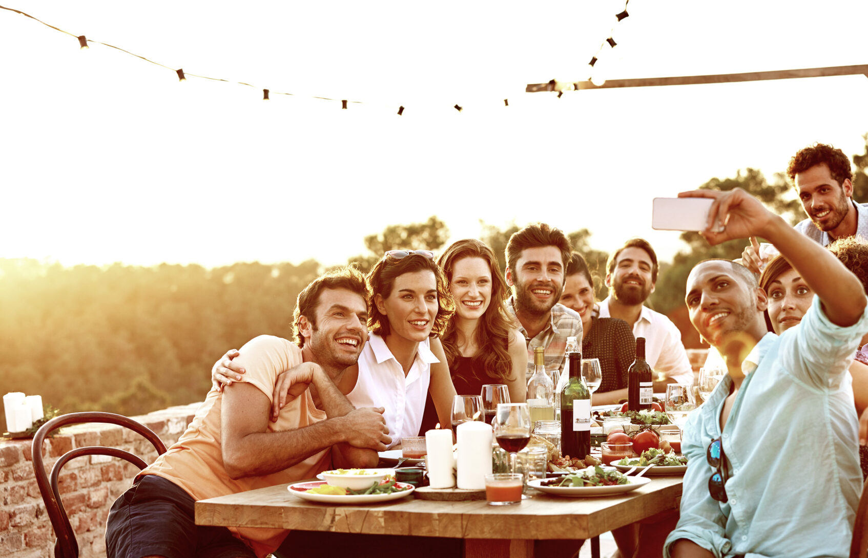 Smiling man taking group selfie on mobile phone at dinner party