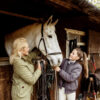 A woman and her daughter standing next to a horse in their stable.