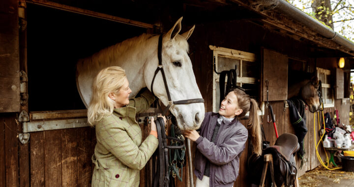 A woman and her daughter standing next to a horse in their stable.