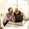 A senior couple looking at a laptop in the kitchen.