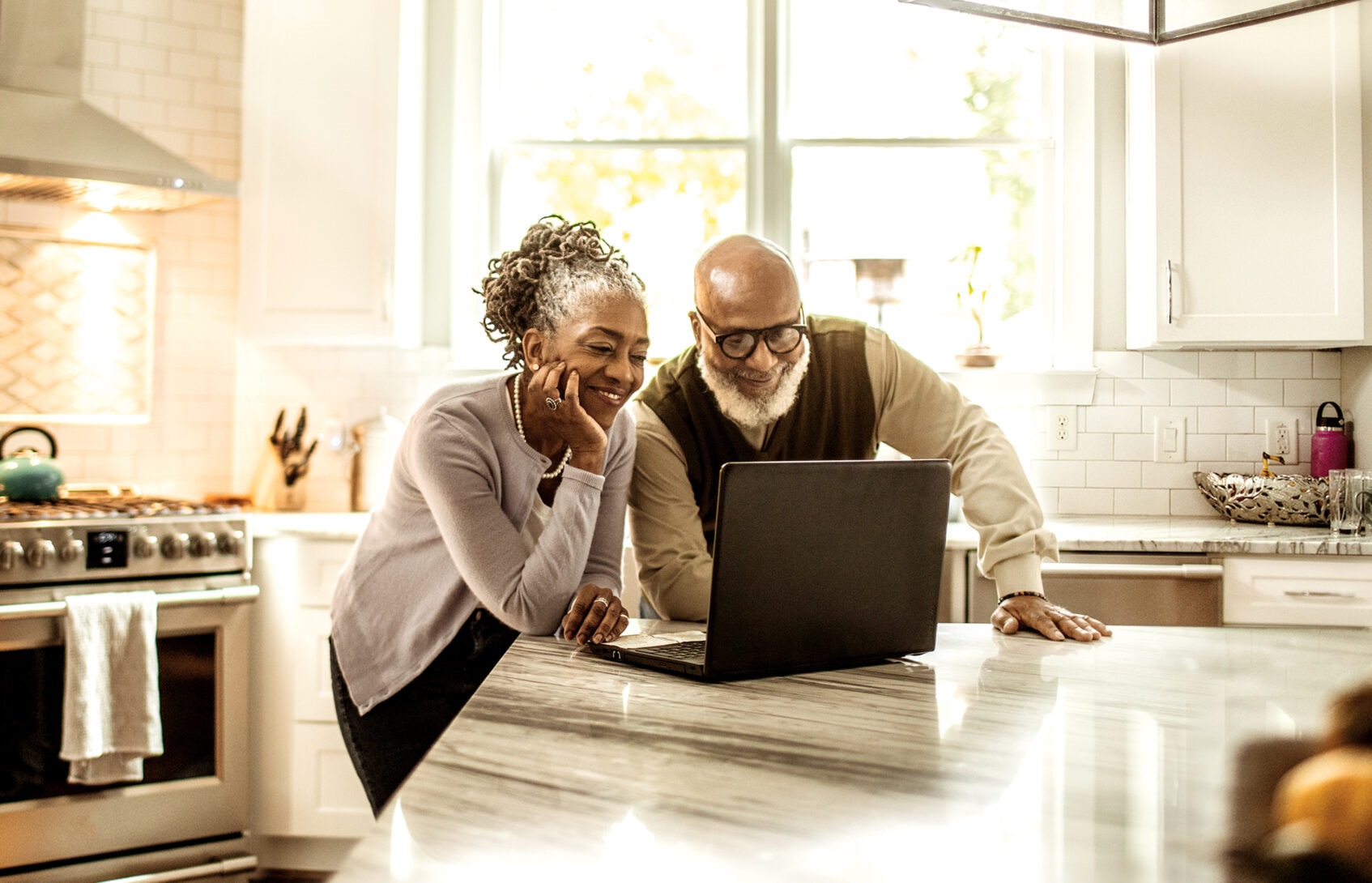 A senior couple looking at a laptop in the kitchen.