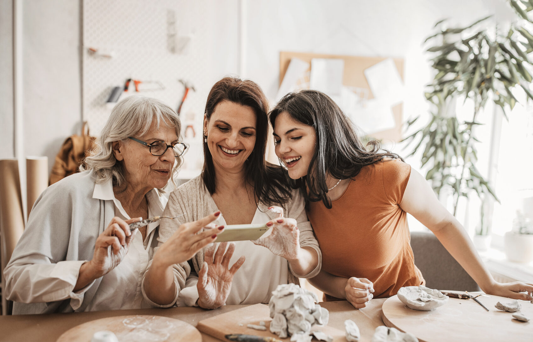 Multigenerational family women taking pictures of their pottery artwork with smartphone.