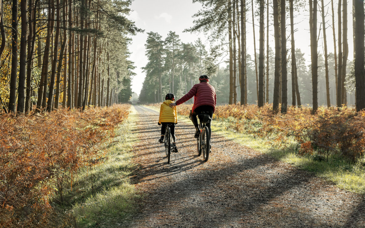 A young girl and father cycling in the forest.