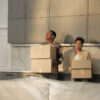 A contemplative married couple is holding moving boxes in their kitchen.