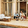 Father and adult son in discussion while relaxing with family on poolside terrace of villa