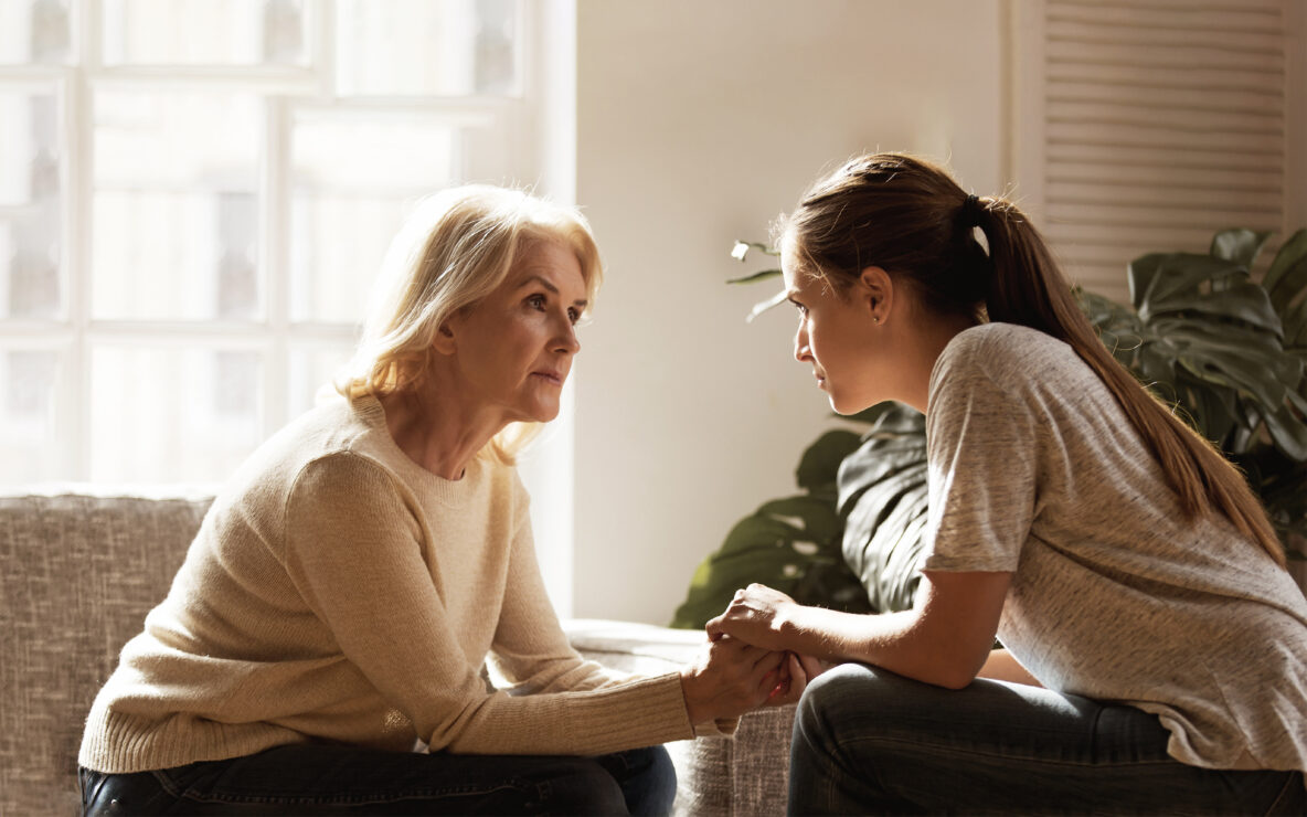 A mother and daughter seated across from each other and holding hands.