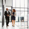 Two business people using a digital tablet while walking in an office.