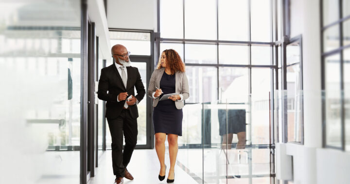 Two business people using a digital tablet while walking in an office.