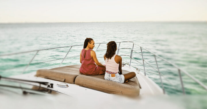 Mother and daughter relaxing on bow of yacht at sunrise during family vacation.