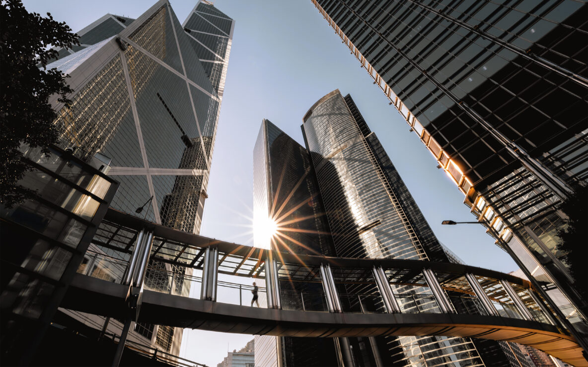 Person walking on footbridge connecting modern office buildings.