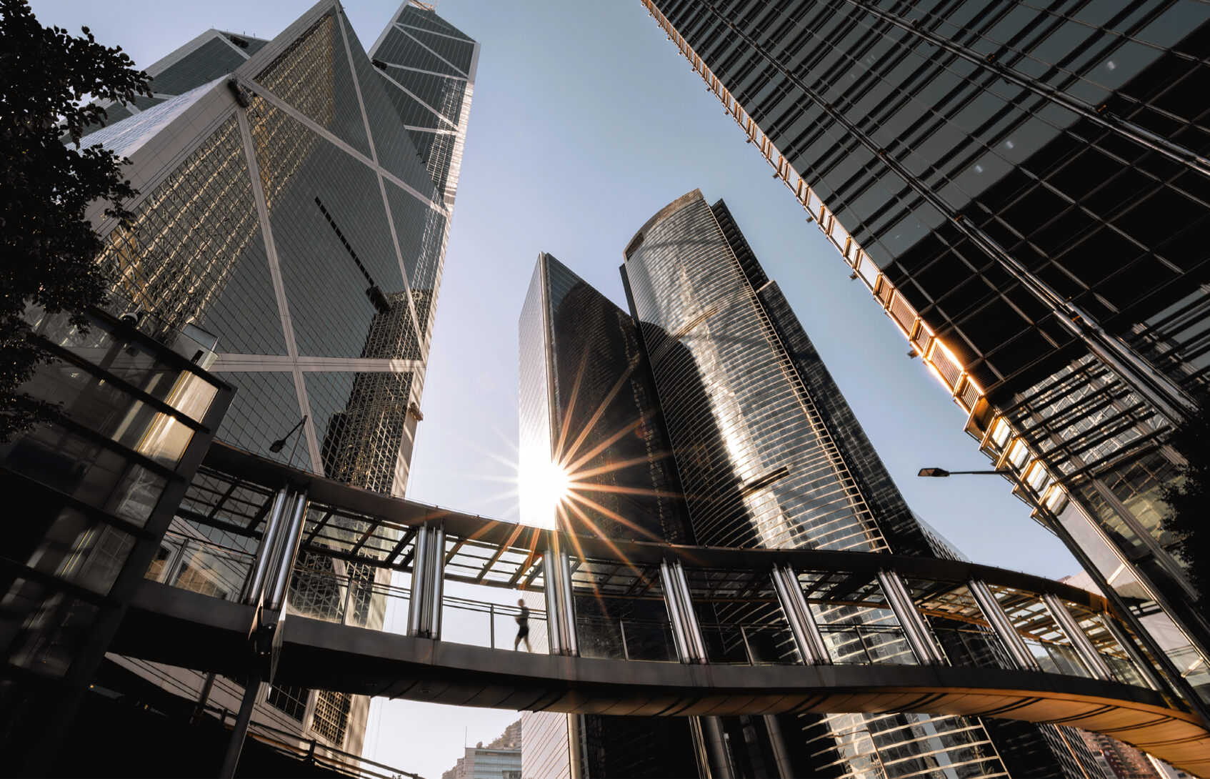 Person walking on footbridge connecting modern office buildings.
