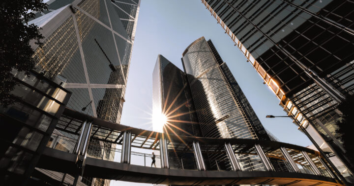 Person walking on footbridge connecting modern office buildings.